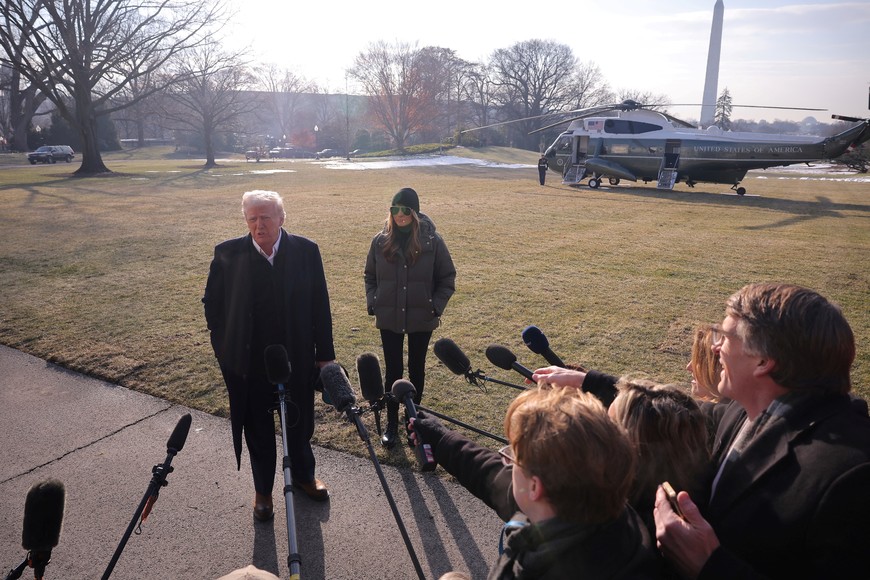 U.S. President Donald Trump speaks to the media, next to first lady Melania Trump, during departure from the White House for his first trip as the new president, in Washington, U.S., January 24, 2025. REUTERS/Carlos Barria