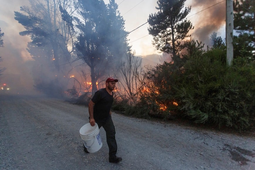 A man walks with a bucket as fire burns trees during a wildfire in Epuyen, in the Patagonian region of Chubut, Argentina January 15, 2025. REUTERS/Matias Garay